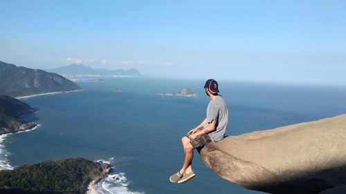 Man sitting on rock over sea against sky