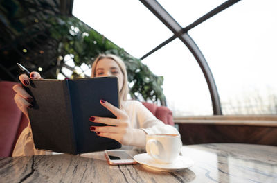 Woman holding coffee cup with mobile phone in cafe