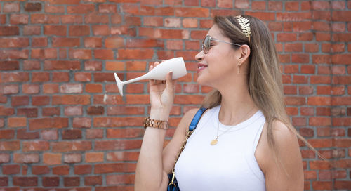 Young woman holding glass with cold bubbly, stands in street cafe on sunny day