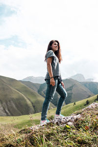 Full length of young woman standing on mountain against sky