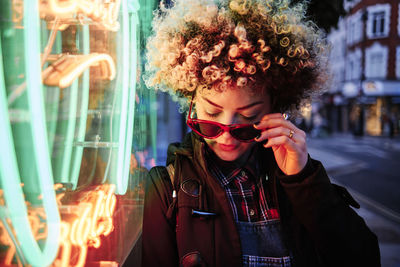 Portrait of smiling young woman standing against illuminated building