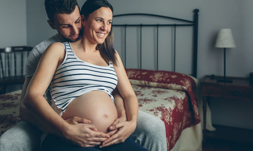 Man embracing pregnant women while sitting on bed at home