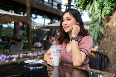 Smiling woman drinking iced coffee while sitting on cafe