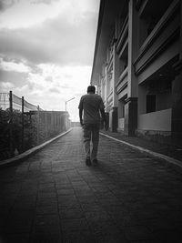 Rear view of man walking on footpath against sky