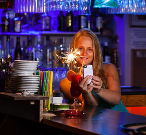 Smiling woman using mobile phone by illuminated drink at restaurant