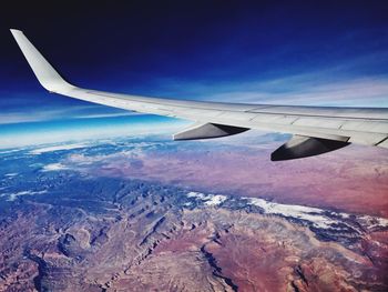 Aerial view of airplane wing over landscape against blue sky
