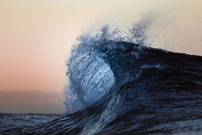 Close-up of sea waves splashing against sky during sunset