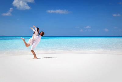 Side view of man lifting woman at beach 