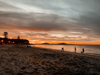 People on beach against sky during sunset