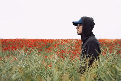 Side view of young man looking away on field against clear sky