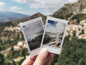 Close-up of hand holding photographs against landscape