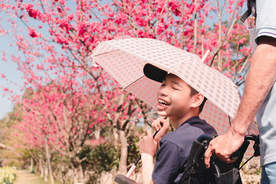 Low angle view of boy looking at pink flower tree