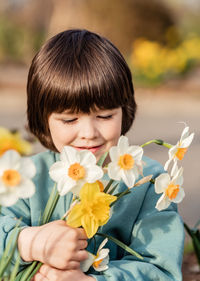 Cute little toddler boy holding spring bouquet of white and yellow daffodil flowers picked in garden 