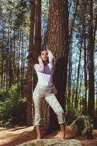 Portrait of young woman standing by tree trunk in forest