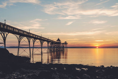 Silhouette bridge over sea against sky during sunset