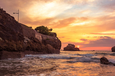 Rock formation on beach against sky during sunset