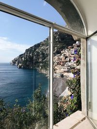 Buildings by sea against sky seen through window