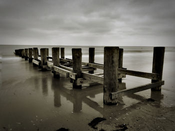 Wooden posts on pier over sea against sky