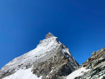 Low angle view of snowcapped mountains against clear blue sky