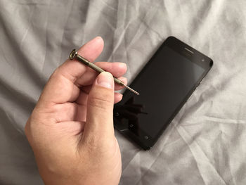 Cropped hand holding nail over mobile phone on bed