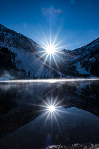 Scenic view of lake and mountains against bright sun during winter