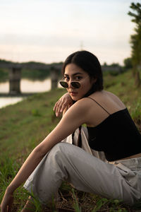 Young woman looking away while sitting on field