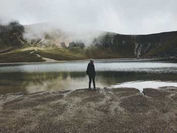 Woman standing at lakeshore against mountains