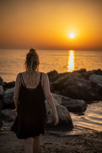 Rear view of woman standing on beach during sunset