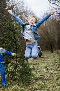 Portrait of girl with brother jumping on field