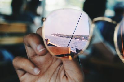 Cropped hand holding sunglasses in boat with reflection of sea