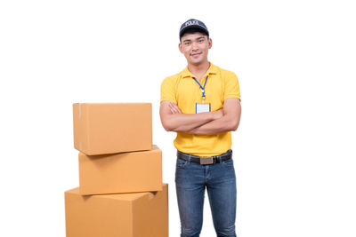 Portrait of smiling delivery man standing by packages against beige background