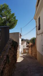 Alley amidst buildings against clear blue sky