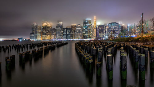 Illuminated modern buildings by river against sky in city at night