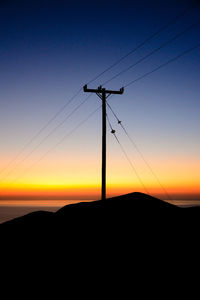Silhouette electricity pylon against orange sky