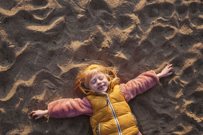 Playful girl with blond hair lying on sand