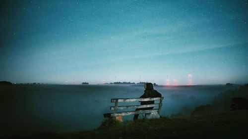 People sitting on bench by lake against sky at night