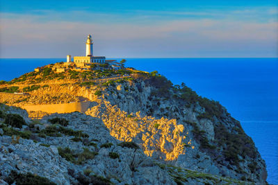 Lighthouse on rock by sea against sky