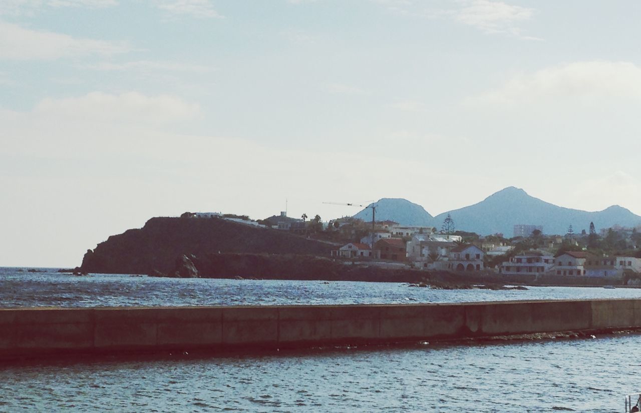 water, architecture, built structure, mountain, building exterior, waterfront, sea, sky, house, mountain range, scenics, nature, tranquil scene, cloud - sky, day, tranquility, residential structure, rippled, cloud, beauty in nature