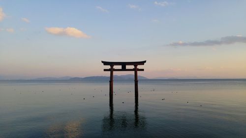Torii gate in calm lake against sky during sunset