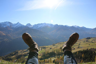 Low section of man relaxing on mountain against sky