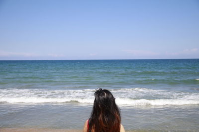 Rear view of woman at beach against sky