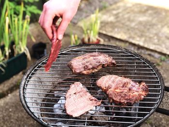 Cropped hand cooking meat on barbecue grill