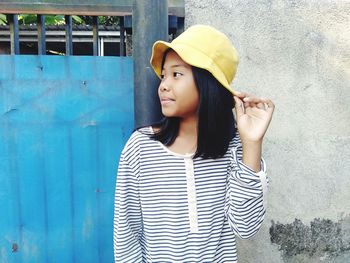 Young woman looking away while standing against wall