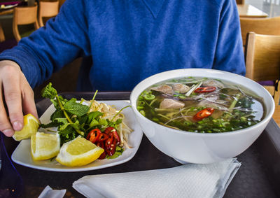 Midsection of person holding lemon slice on table in restaurant