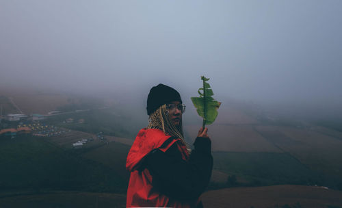 Side view of woman standing on mountain against sky during foggy weather