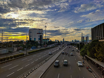 Vehicles on road against sky during sunset in city