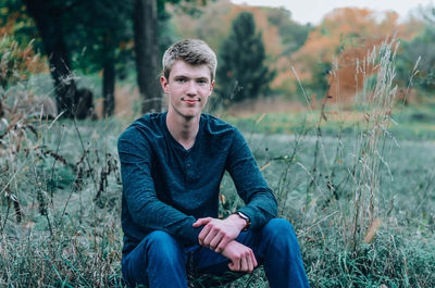 Portrait of young man sitting on grassy land