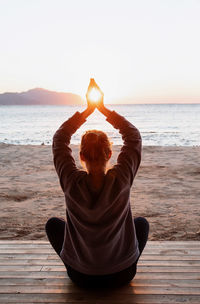 Rear view of woman sitting on beach in yoga position