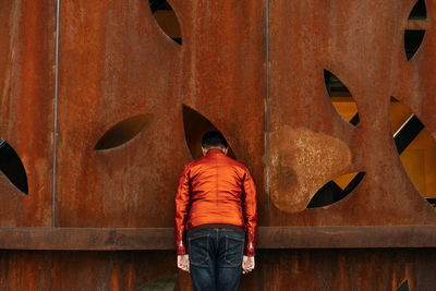 Rear view of man standing against orange rusty wall