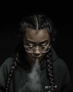 Close-up of woman smoking while standing against black background